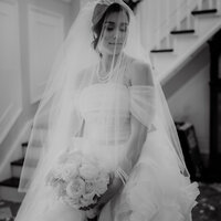 Mariée en robe blanche et voile, tenant un bouquet de fleurs, portrait en noir et blanc dans un escalier