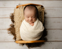Sleeping newborn baby wrapped in a cream swaddle and posed in a wooden prop bed during a studio newborn photography session with newborn photographer Kaitlyn Dawn Photography.