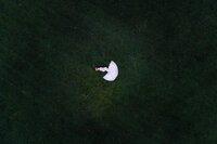 An aerial photograph of a pregnant mother lying on her side in a large open field.