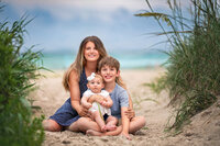 Mother sitting with her two children along a sandy beach path near Atlantic Beach NC during sunset family session