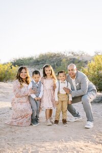 The Collins family smiling together in the Las Vegas desert, with parents kneeling beside their three young children during a warm golden hour outdoor family portrait session.