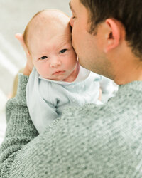 Father kissing his newborn baby’s head during a tender in-home newborn photography session.