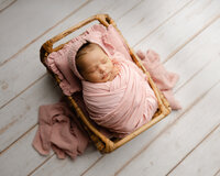 Sleeping newborn baby girl wrapped in a blush pink swaddle and posed in a wooden crate prop during a studio session with newborn photographer Kaitlyn Dawn Photography.