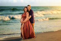 Expectant couple embracing on the shoreline during a sunset maternity session in Atlantic Beach North Carolina