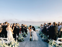 A celebratory dip kiss between a bride and groom on a rooftop overlooking the ocean at Wychmere Beach Club in Cape Cod.