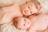 Big brother smiling while holding newborn baby boy in soft studio setting