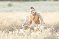 A father posing next to his son at a local Dallas park as they both look and smile at their family photographer.