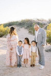 The Collins family sharing a candid moment in the Las Vegas desert, with parents looking at their three children standing together in soft golden hour light during a relaxed outdoor family photo session.