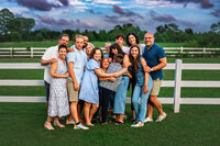 Multigenerational family hugging together in front of a white fence during a farm family session in New Bern North Carolina