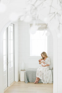 a mother and her baby sitting in a bright room and cuddling with each other