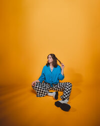 Creative portrait of Morgan Wright in a blue outfit against a warm orange backdrop.