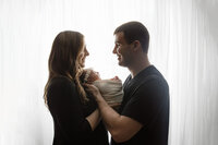 A couple poses with their newborn girl in front of a white backlit curtain at Jennifer Brandes Photography studio, New Ulm, MN.