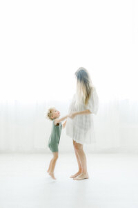 A portrait taken in a DFW photography studio of a pregnant mother dancing around with her toddler son for her maternity session.