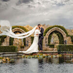 Bride and groom embracing beside the reflecting pool at Allerton Castle, Yorkshire, with flowing veil captured by Yorkshire wedding photographer.