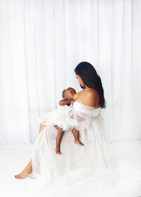 Mother nursing baby girl wearing white gown during mommy and me mini session photoshoot in Mt. Juliet tennessee photography studio
