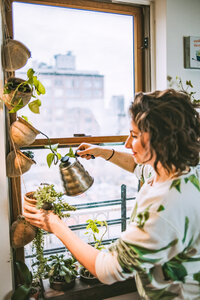Maria tends to her hanging potted plants hanging in her apartment window
