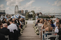 Cérémonie de mariage en plein air sur une terrasse dominant le fleuve, arche florale, allée bordée de fleurs blanches, grande roue et pont Jacques-Cartier en arrière-plan au Grand Quai de Montréal