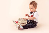 toddler reaching toward simple frosted cake during first birthday cake smash
