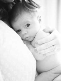 Black and white lifestyle newborn photo of a baby resting against mom’s shoulder during an in-home newborn session.