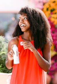 Model in a coral dress with Evian facial spray in front of flowering bougainvillea