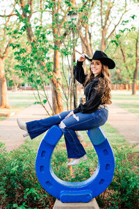 Girl wearing jeans and a black top sitting on the MTSU horseshoe wearing a cowboy hat
