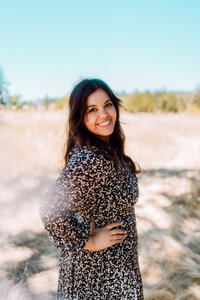 Musician smiling outdoors in a black floral dress during a creative brand photography session