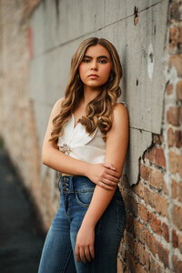 Senior portrait in downtown Mobile, Alabama — leaning against a brick wall wearing blue jeans.