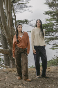 Rust cardigan and cream crewneck sweater styled with corduroy trousers among the cypress