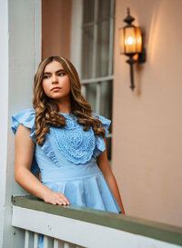 Senior portrait at the Malaga Inn in Mobile, Alabama— in the courtyard leaning against a while wooden post and looking off in the distance.