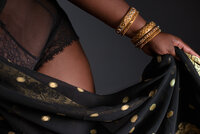 Close detail of a hand gathering black and gold sari fabric against skin, stacked gold bangles at the wrist.