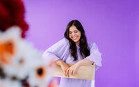 Musician seated against a purple backdrop with colorful flowers during a playful brand photoshoot