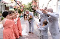 Jacksonville, FL wedding photographer capturing a St. Augustine wedding in a joyful street celebration as the bride and groom kiss in the center of a historic brick lane, wedding party and children reaching in around them.