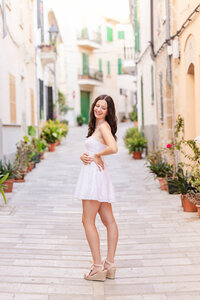 Travel portrait session in Mallorca—young woman in a white dress standing on a charming European street