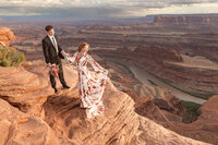 groom holding brides hand while looking off in distance on rocks at dead horse state park