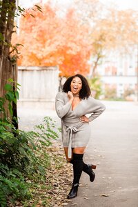 Girl wearing black boots, grey sweater wrap dress and laughing at the camera