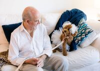 In St. Augustine, the father of the bride smiles at the family dog wearing a white tulle skirt and bow, a beloved “bridesmaid” waiting before the ceremony. - A portrait experience by Nature's Child Photography.