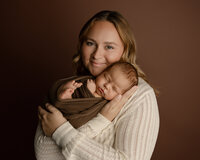 Mother cuddling her sleeping newborn baby wrapped in a brown swaddle during an emotional newborn family photography session by Inland Empire newborn photographer Kaitlyn Dawn Photography.