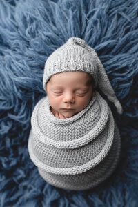 Newborn boy wrapped in a knit blue wrap with a matching sleepy cap during his newborn photography session near Mankato, Minnesota.