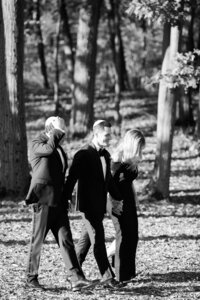 the groom walking hand-in-hand with a woman in a black gown and another man in a tuxedo