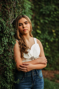 Senior portrait in downtown Mobile, Alabama — closeup of her leaning into the greenery looking into the camera with a soft smile.