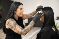 Tattooed beauty professional smiling while styling a client’s brows. Photograph by Yucaipa branding photographer Kaitlyn Dawn Photography.