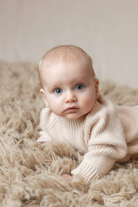Baby boy with big blue eyes wearing a chunky cream sweater for his baby milestone portrait session in South Central Minnesota.