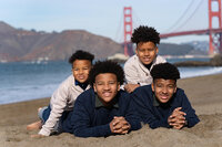 Family of four boys posing on the beach with the golden gate bridge in the background