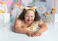 Jacksonville, FL portrait session capturing Joyful young girl with curly hair wearing a yellow striped outfit and matching bow headband lying on her stomach and smiling brightly during a studio child portrait session in Mandarin.