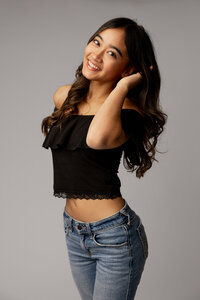High school senior girl with long dark hair wearing a black top and jeans posing in a studio, studio senior portrait by Kaitlyn Dawn Photography.