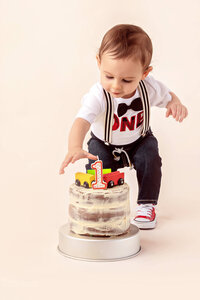 toddler reaching toward simple frosted cake during first birthday cake smash