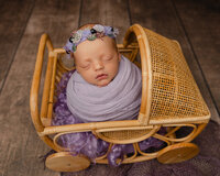 Newborn baby wrapped in soft purple tones resting in a wicker cradle. Photographed by Inland Empire newborn photographer Kaitlyn Dawn Photography.