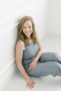 A professional headshot of a Dallas business woman sitting on the floor of a photography studio looking up and smiling at the photographer as she captures her.