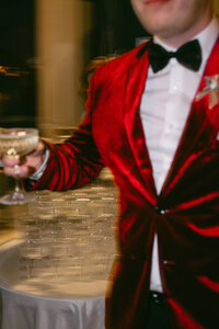 Stylish groom in red velvet suit with glass of champagne on the party