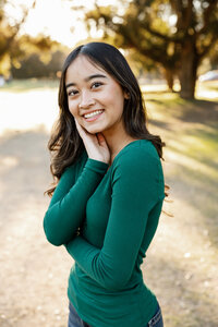 Close-up portrait of a smiling high school senior girl in a green top with warm sunset light, senior photography by Kaitlyn Dawn Photography.